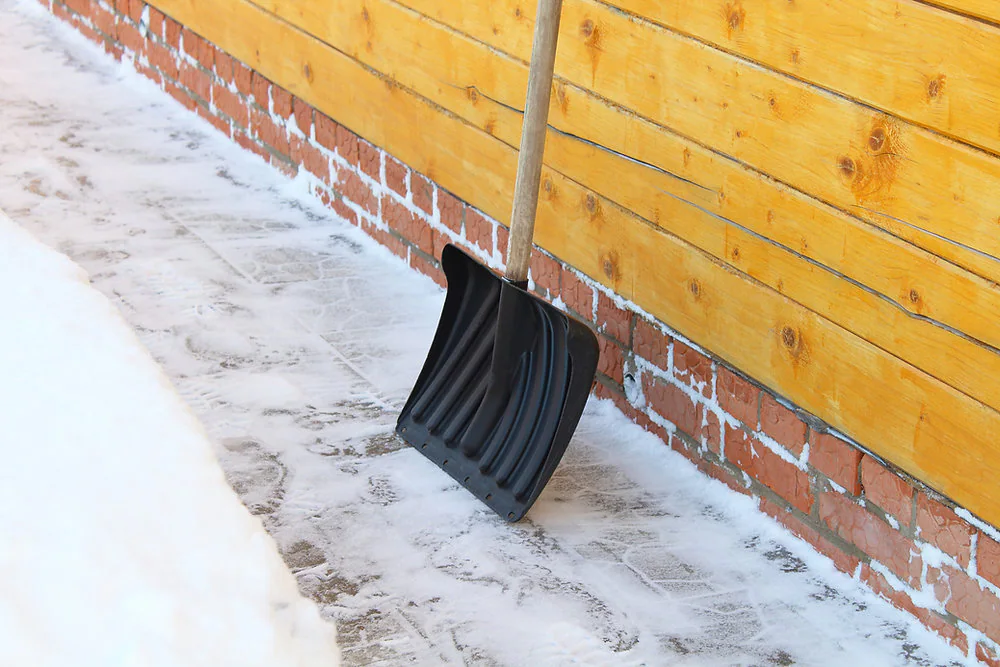Snow shovel clearing frozen ground beside a wooden building