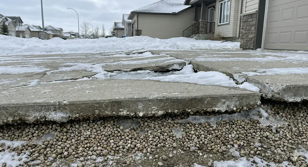 Exposed gravel base beneath a frost-heaved concrete driveway
