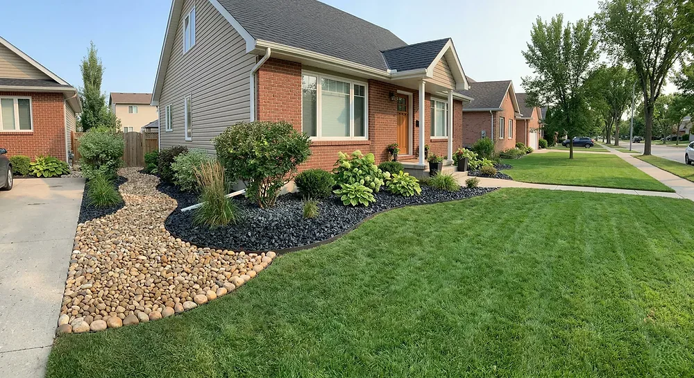 Winnipeg garden bed with black granite decorative stone showing high contrast modern landscape design against green plants