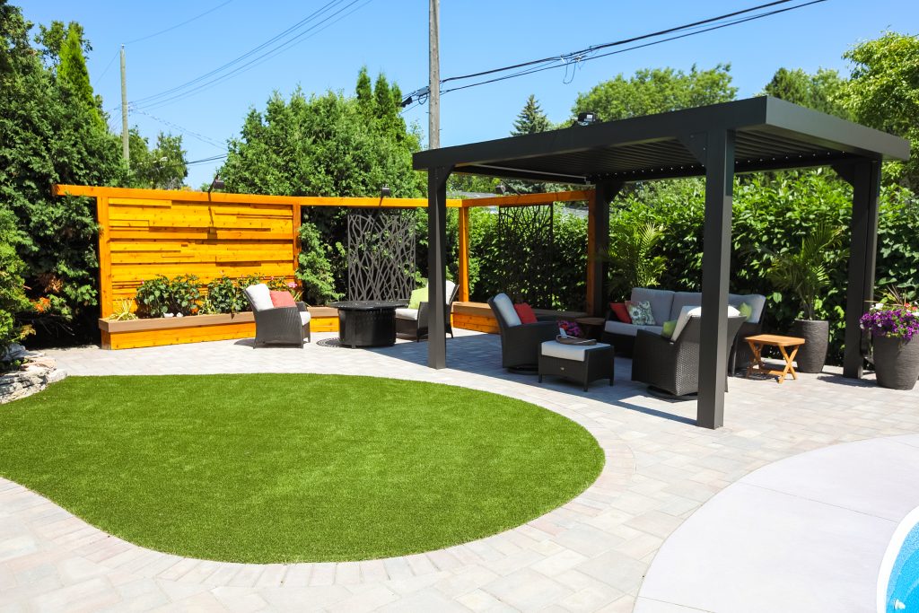 Synthetic turf lawn beside a backyard paver patio and pergola